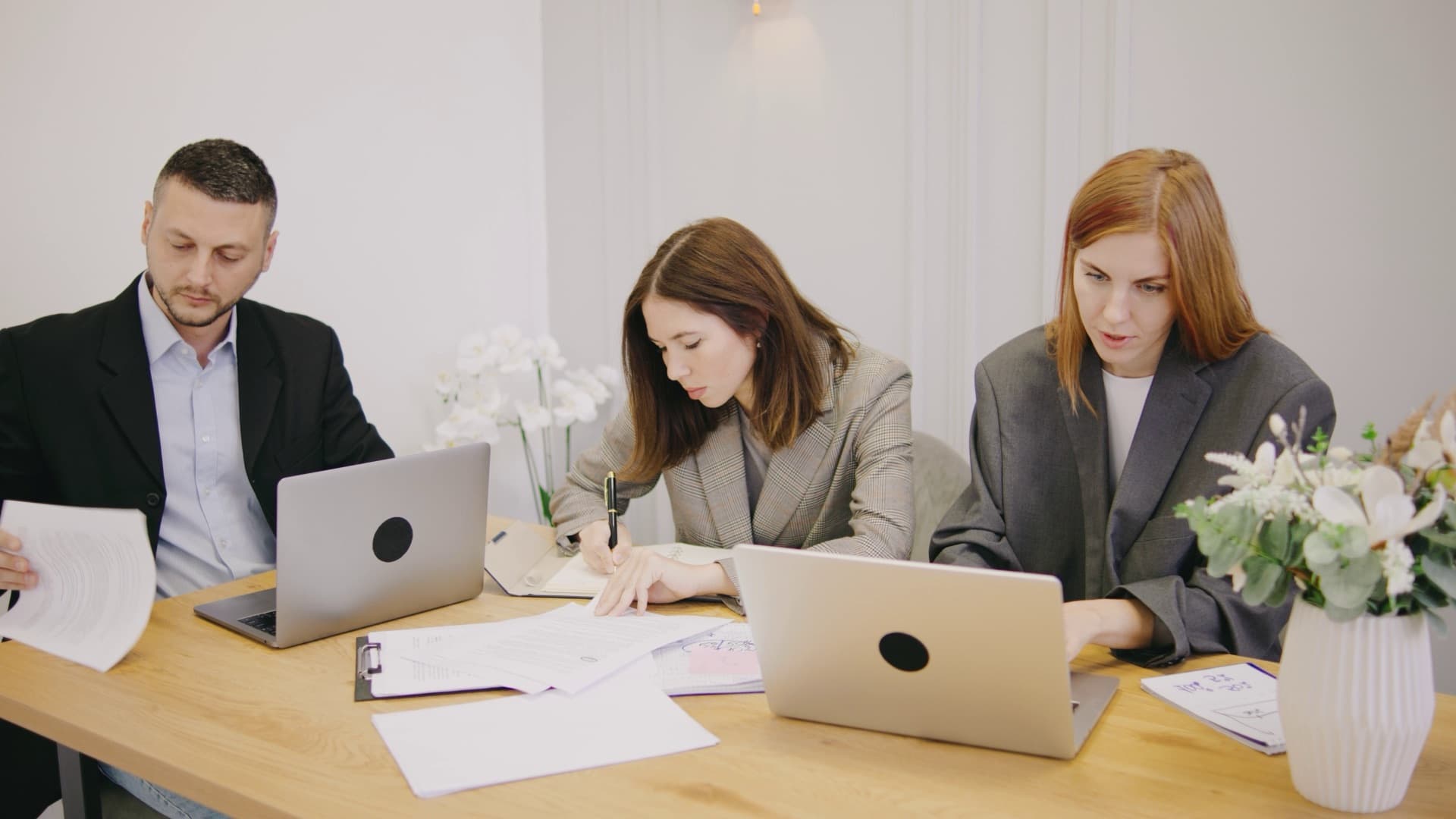 Three colleagues working through documents and laptops at a shared table
